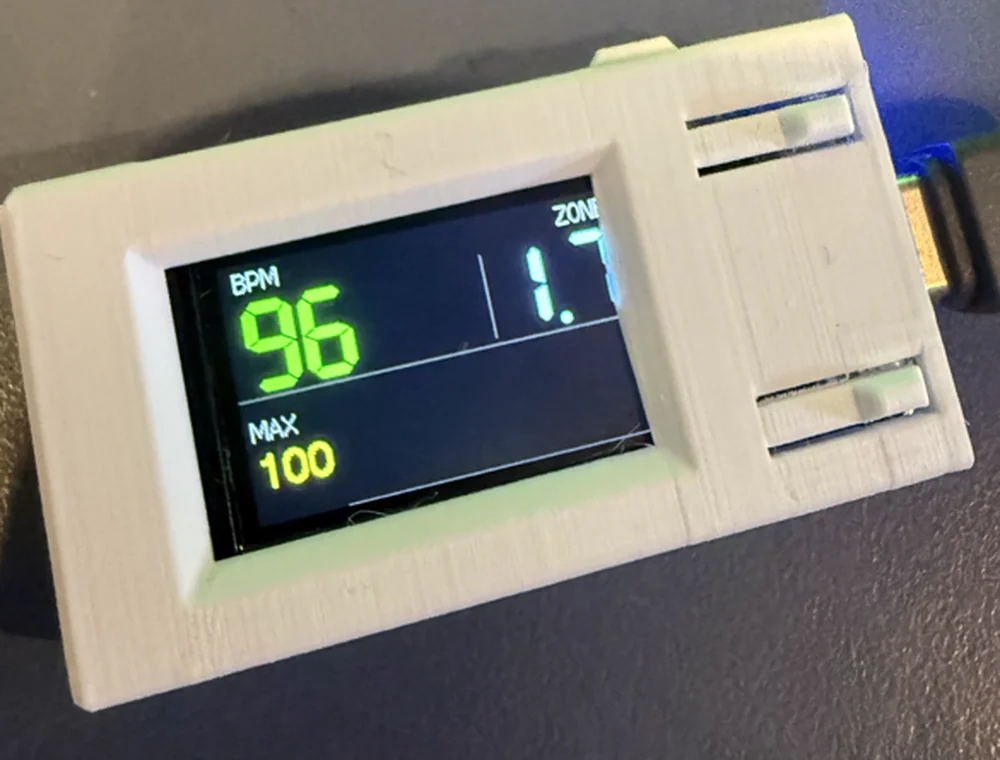 The HeartHertz prototype in a 3D-printed wall-mounted case, showing BPM 96, ZONE 1.7 and MAX 100 on a small colour display
